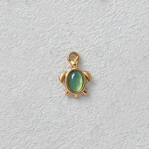 Detailed macro view of a gold-plated turtle pendant featuring a green oval gemstone inlay