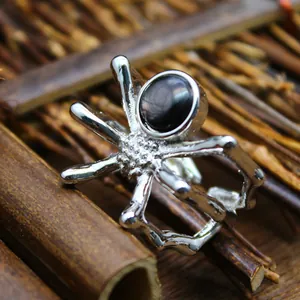 Close-up macro view of a silver spider-shaped ring featuring a polished dark natural stone inlay.