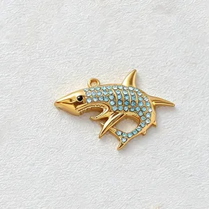 Close-up of a gold-plated shark pendant featuring sparkling light blue crystal inlay detail