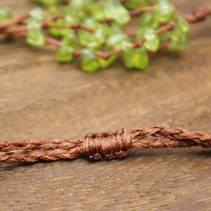 Macro detail of handmade brown woven cord knot with green peridot stones background.