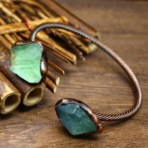 Close-up detail of a vintage open bangle with raw green gemstones and a twisted copper band.