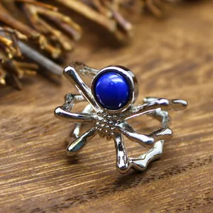 Macro detail of a silver spider open ring with a round blue natural stone on wood.