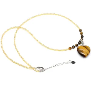 Detailed view of the natural tiger eye heart pendant on a yellow seed bead necklace.