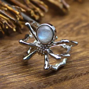 Macro detail of a spider-shaped open ring with a glowing round gemstone on wood.
