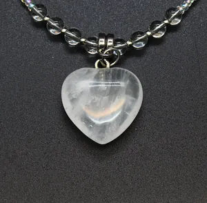 Close-up detail of clear heart-shaped stone pendant with iridescent bead chain.