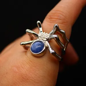 Macro view of a silver spider-shaped open ring featuring a blue natural kyanite gemstone.