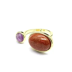 Gros plan d'une bague rétro en or avec une pierre goldstone ovale et un cristal violet rond.