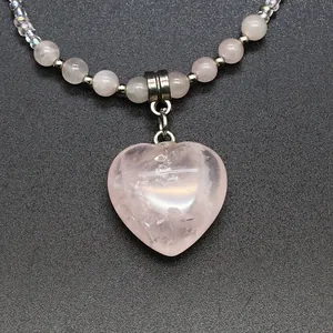 Close-up detail of a delicate pink natural stone heart pendant on a beaded necklace chain.