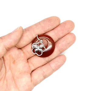 Pendentif donut en agate rouge avec breloque papillon argentée dans la main