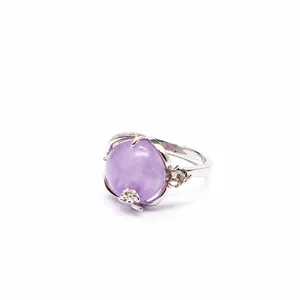 Gros plan d'une bague argentée avec une grande pierre violette et des détails floraux.