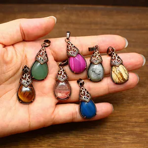 Detailed view of vintage teardrop stone pendants held in hand with copper filigree caps.