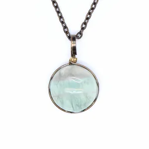 Close-up detail of a round light green natural stone pendant with a vintage metal frame
