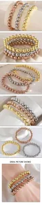 Vista detallada de pulseras de cuentas de acero en oro, plata y oro rosa apiladas en muñeca.