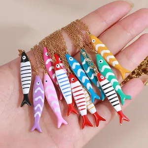 Hand holding multiple colorful enamel fish pendants on gold stainless steel necklaces