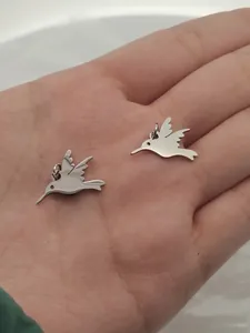 Macro view of stainless steel hummingbird charms held in hand showing scale