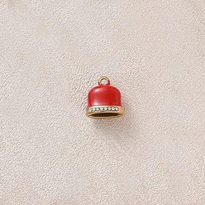 Close-up of a red enamel bell charm with sparkling rhinestone trim and a gold loop.