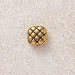 Makroansicht einer vergoldeten Edelstahlperle mit gestepptem Ananasmuster für DIY-Schmuck.