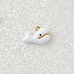 Close-up view of a minimalist white enamel whale pendant with gold-plated steel details