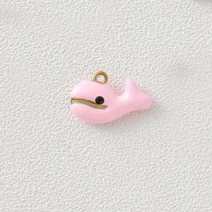 Close-up detail of a cute pink enamel whale charm with gold-plated loop for DIY jewelry