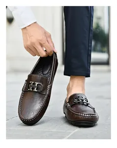 Homme montrant un mocassin en cuir marron avec boucle en métal et coutures blanches