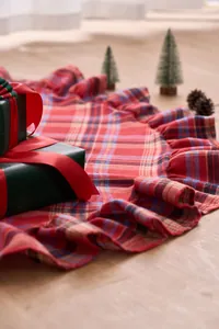 Close-up of red and blue plaid Christmas tree skirt with ruffled edges on wood floor