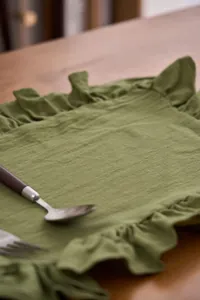 Dettaglio di una tovaglietta verde con volant su un tavolo di legno con posate.