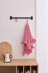 Red and white checkered cotton hand towel with elegant ruffled edges hanging on a wall hook