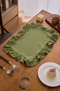 Tovaglietta verde con volant su tavolo in legno con posate e dessert per cenare.
