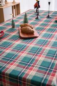 Atmospheric view of a green and red Christmas plaid tablecloth in a rustic setting.