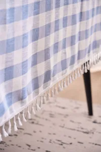 Close-up detail of blue and white checkered linen tablecloth with delicate white tassels.