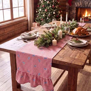 Red checkered Christmas table runner with blue bows and ruffled edges on wooden table