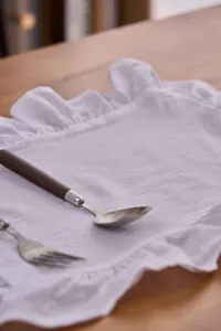 Detailopname van wit katoenen linnen placemat met ruches en zachte textuur.