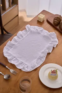 Detail van een wit katoenen linnen placemat met elegante ruche randen op een houten tafel