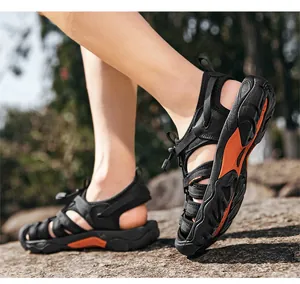 Detailed side view of black and orange outdoor sports sandals with elastic drawstring closure on rocks