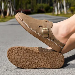 Close-up of brown suede loafers showing decorative stitching, buckle strap and textured sole.