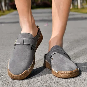 Close-up detail of grey suede loafers featuring white hand-stitching and buckle strap