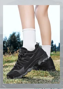 Detailed side view of breathable black outdoor hiking shoes worn on a grassy natural trail