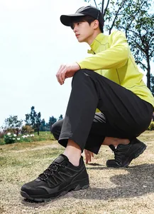 Male model wearing black trekking shoes squatting on grass in a daylight outdoor setting