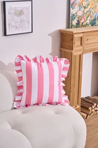 Close-up detail of a pink and white ruffled stripe cushion on a white sofa in a cozy room.