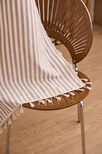 Detalle de cortina a rayas caqui con borlas sobre una silla de madera rústica.