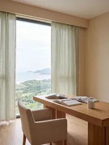 Primer plano de cortinas de rayas verdes con borlas en una estancia luminosa frente al mar.