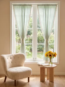 Salbeigrüne Gingham-Fenstervorhänge mit Quastenbesatz in einem gemütlichen Sonnenzimmer.