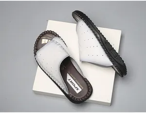 Détail de claquettes en cuir blanc respirant avec semelle marron souple et logo sport.