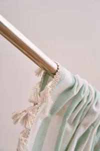 Close-up of striped cotton linen curtain with elegant cream tassels on a metal rod.