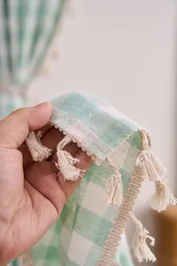 Close-up of sage green gingham cotton linen curtain with handmade tassel fringe details.