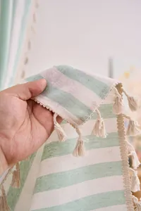 Close-up of mint green striped cotton linen curtain with decorative tassel fringe