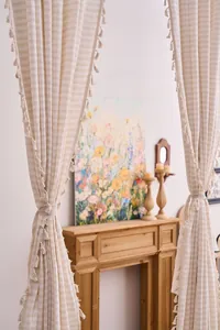Dettaglio tenda in cotone crema con nappe e motivo a righe in casa.