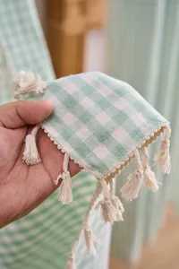 Detailansicht von salbeigrünem Gingham-Vorhangstoff mit dekorativen cremefarbenen Quasten