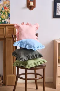 French ruffle edge cotton cushion covers in assorted soft colors stacked on a chair.