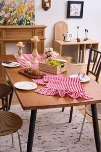 Detail of red checkered table runner with elegant ruffled edges on a wooden dining table.